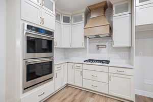 Kitchen featuring stainless steel appliances, light wood finished floors, backsplash, and white cabinetry