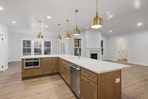 Kitchen with wood finish cabinets, light wood finished floors, open floor plan, stainless steel appliances, and a fireplace