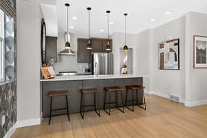 Kitchen featuring a peninsula, a kitchen breakfast bar, dark wood finish cabinetry, decorative light fixtures, and stainless steel appliances