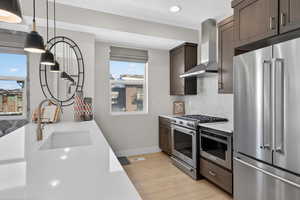 Kitchen featuring stainless steel appliances, light wood-type flooring, backsplash, light stone counters, and decorative light fixtures