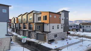 Snow covered property with stone siding, a garage, a residential view, and a mountain view