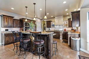 Kitchen with dark wood finish cabinetry, arched walkways, light stone countertops, a breakfast bar area, and a kitchen island