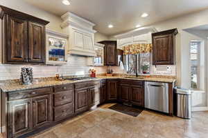 Kitchen featuring dark wood finish cabinetry, stainless steel appliances, light stone counters, decorative backsplash, and recessed lighting