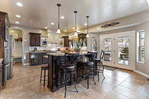 Kitchen with dark wood finish cabinetry, light stone countertops, arched walkways, a breakfast bar area, and hanging light fixtures
