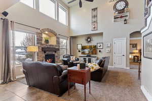Carpeted living area with a fireplace, a ceiling fan, a baseboard radiator, a high ceiling, and arched walkways