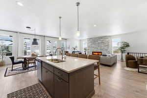 Kitchen featuring dark wood finish cabinetry, light wood-style floors, pendant lighting, and a stone fireplace