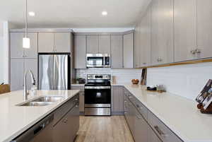Kitchen with hanging light fixtures, stainless steel appliances, light wood finished floors, decorative backsplash, and light stone counters