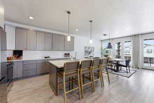 Kitchen featuring decorative light fixtures, a breakfast bar, light wood finished floors, electric range, and backsplash