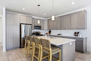 Kitchen with stainless steel appliances, gray cabinetry, a kitchen bar, and hanging light fixtures