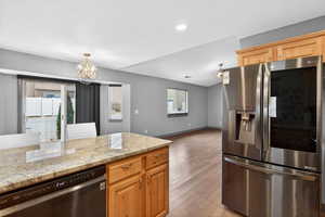 Kitchen featuring stainless steel fridge with ice dispenser, light stone countertops, dishwasher, light wood-style floors, and suspended lighting