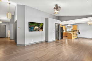 Unfurnished living room featuring hanging lights, light wood-type flooring, and vaulted ceiling