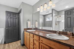 Bathroom featuring double vanity, a stall shower, and light wood-type flooring