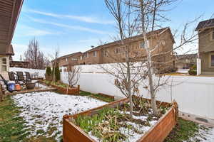 Yard layered in snow with a vegetable garden and a fenced backyard