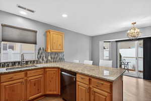Kitchen featuring decorative backsplash, light stone counters, dishwasher, and a peninsula