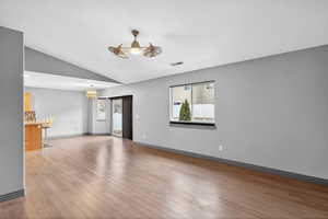 Unfurnished living room with light wood-style flooring, lofted ceiling, and suspended lighting