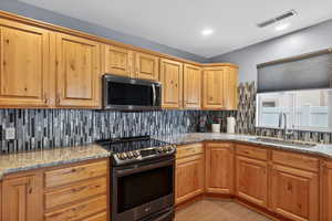 Kitchen featuring stainless steel appliances, light stone countertops, and backsplash