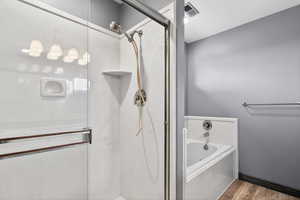 Full bathroom featuring a marble finish shower, a garden tub, and wood finished floors