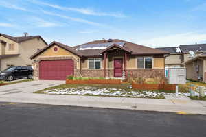 View of front of property featuring solar panels, an attached garage, stucco siding, driveway, and stone siding