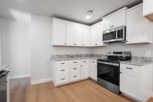 Kitchen featuring stainless steel appliances, light wood-type flooring, light stone counters, white cabinetry, and recessed lighting