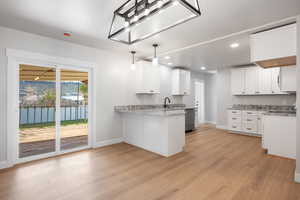 Kitchen featuring light stone counters, white cabinetry, a peninsula, and light wood-type flooring