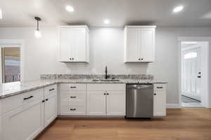 Kitchen featuring white cabinets, stainless steel dishwasher, light stone countertops, and light wood finished floors