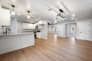 Kitchen featuring arched walkways, range with electric stovetop, pendant lighting, and white cabinetry