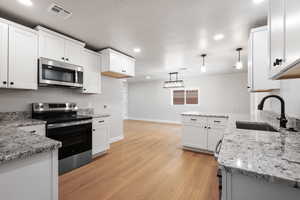 Kitchen with stainless steel appliances, light stone countertops, white cabinetry, and decorative light fixtures