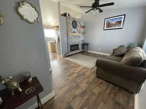 Living area with dark wood-type flooring, vaulted ceiling, a ceiling fan, and a fireplace