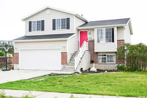 Split level home with an attached garage, brick siding, concrete driveway, a front lawn, and a shingled roof