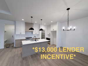 Kitchen with dual tone cabinetry, a center island with sink, light wood-style flooring, stainless steel gas range oven, and a chandelier