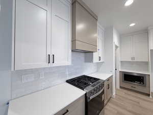 Kitchen featuring stainless steel appliances, two tone cabinetry, recessed lighting, decorative backsplash, and light stone countertops