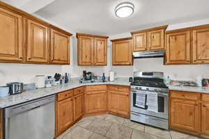 Kitchen with stainless steel appliances, wood finish cabinetry, light stone counters, and a textured ceiling