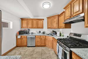 Kitchen featuring stainless steel appliances, wood finish cabinets, a textured ceiling, light stone countertops, and beamed ceiling