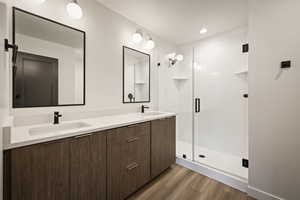 Full bath with double vanity, dark wood-style flooring, a shower stall, and recessed lighting