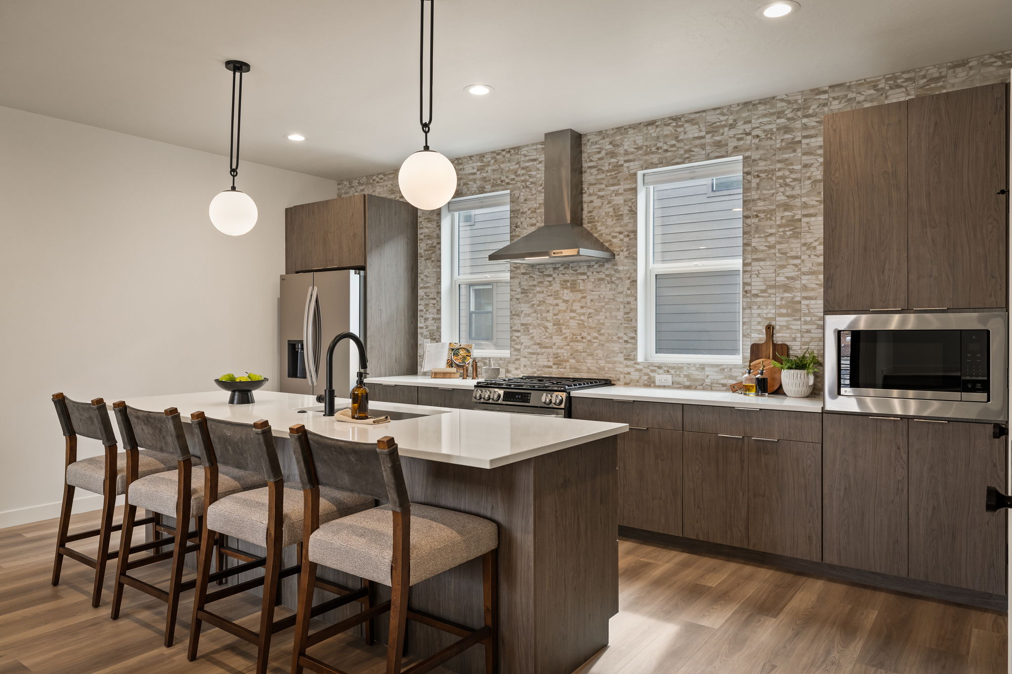 Kitchen featuring modern cabinets, a breakfast bar area, backsplash, decorative light fixtures, and a center island with sink