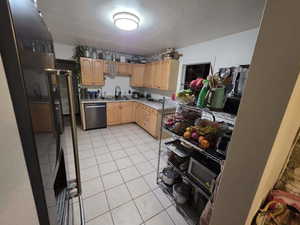 Kitchen with light tile patterned floors, dishwasher, light wood finish cabinetry, light countertops, and freestanding refrigerator