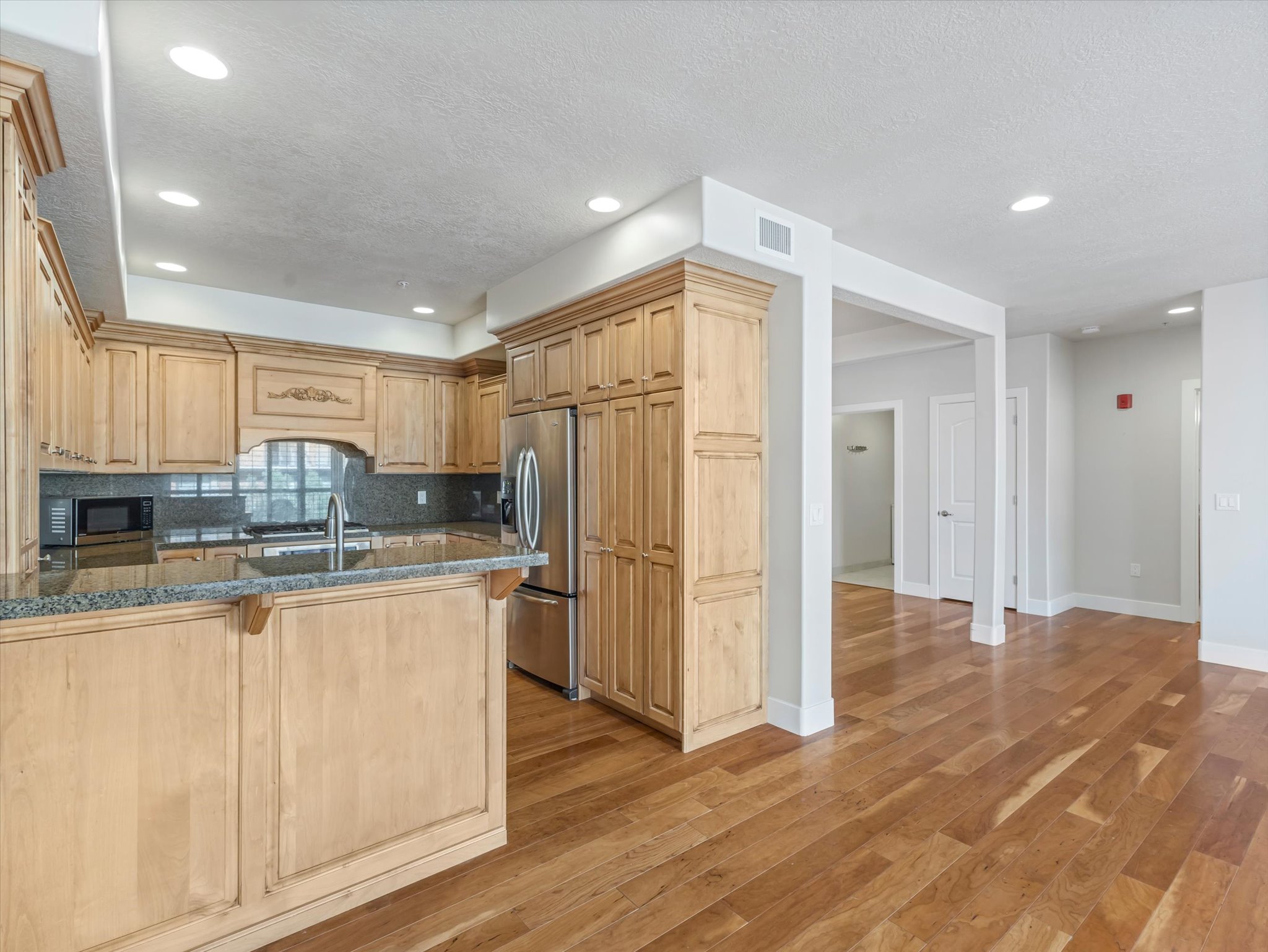 Kitchen with a peninsula, stainless steel appliances, decorative backsplash, light wood-style flooring, and dark stone counters