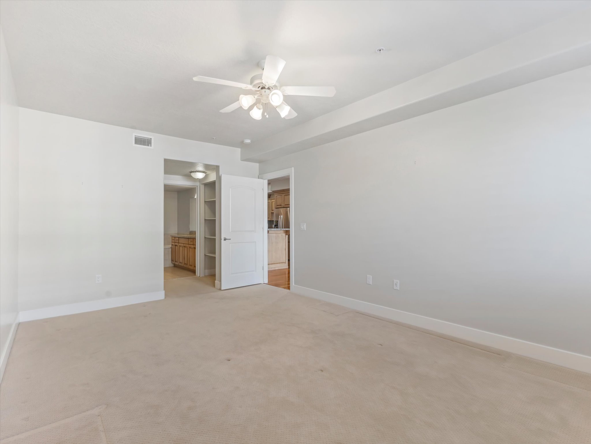 Unfurnished bedroom featuring light carpet, a ceiling fan, ensuite bathroom, and freestanding refrigerator