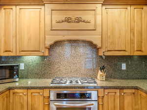 Kitchen with stainless steel appliances, extractor fan, tasteful backsplash, and ample cabinet and pantry space.