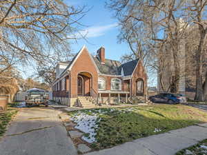 Tudor home featuring brick siding, a front yard, a chimney, and driveway