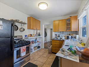 Kitchen with wood finish cabinets, freestanding refrigerator, gas range, open shelves, and glass insert cabinets