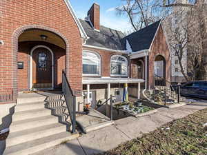 Property entrance with brick siding, a shingled roof, and a chimney