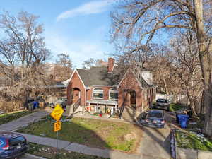 View of front of property featuring brick siding, a porch, a shingled roof, a chimney, and a front yard