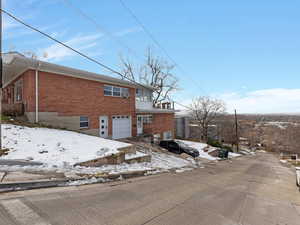 Snow covered back of property featuring an attached garage, brick siding, and a balcony