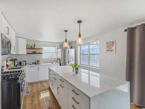 Kitchen with white cabinetry, stainless steel appliances, decorative light fixtures, light wood finished floors, and open shelves