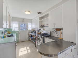 Kitchen featuring open shelves, white cabinetry, range with two ovens, a peninsula, and tile countertops