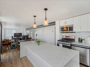 Kitchen with stainless steel appliances, light stone counters, pendant lighting, and light wood finished floors