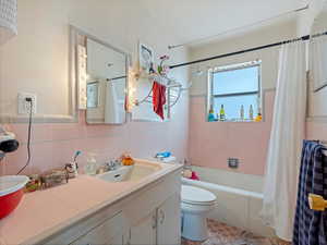 Bathroom featuring tile walls, vanity, shower / tub combo, and wainscoting