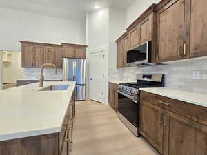 Kitchen with stainless steel appliances, tasteful backsplash, light stone counters, light wood finished floors, and a high ceiling