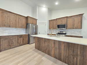 Kitchen with decorative backsplash, stainless steel appliances, wood finish cabinets, light wood finished floors, and vaulted ceiling